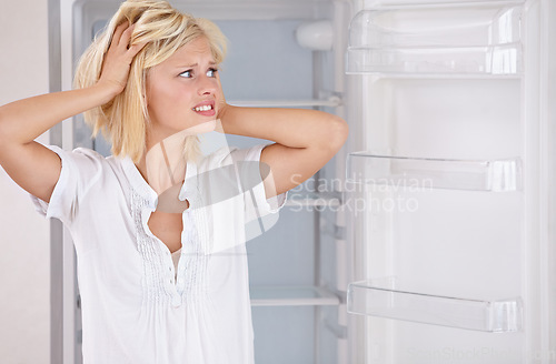 Image of Woman, worried and empty fridge or stress for economic crisis in kitchen for starving problem in home. Female person, unhappy and concern for hungry poverty or frustrated, inflation for eating fail