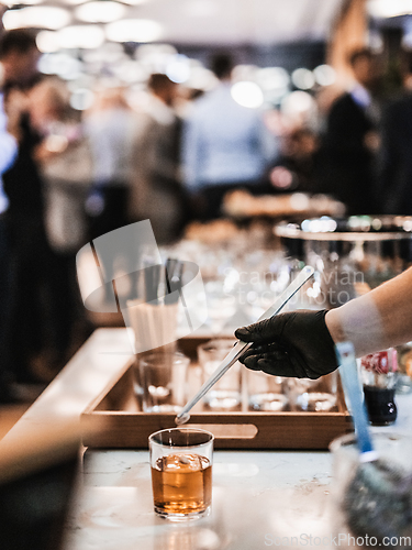 Image of Expert barman is making cocktail at business banquet event in hotel conference center. Blurred businesspeople at banquet event business meeting event in the background