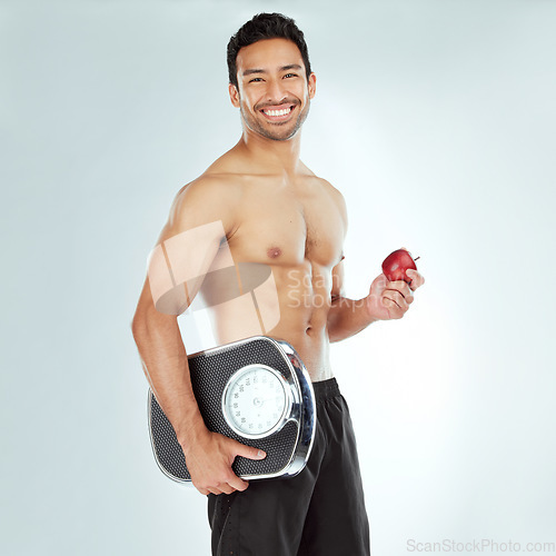Image of Scale, health and portrait of fitness man with apple in studio for Weight loss, diet or detox on white background. Nutrition, balance or face of wellness model smile for superfoods, fruit or progress