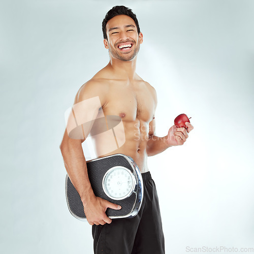 Image of Health, scale and portrait of fitness man with apple in studio for weight loss, diet or detox on white background. Nutrition, balance or face of wellness model smile for superfoods, fruit or progress