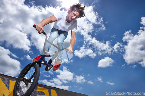 Image of Bike, jump and teen on ramp for sport performance, ride or training for event at park with sky. Bicycle, stunt or kid balance on edge of board for cycling trick in competition or challenge with risk