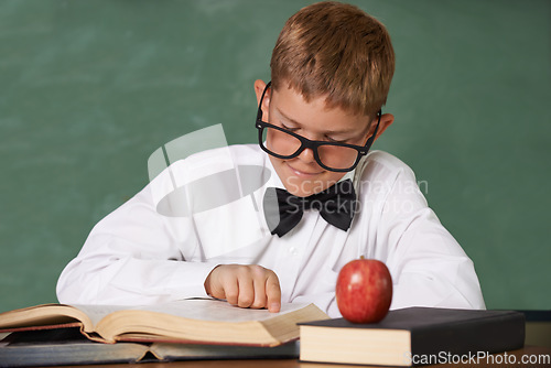 Image of Young boy, book and reading at school for learning, education or knowledge by green chalk board. Male person, smart child or teenager smile with textbook for academic literature or studying in class