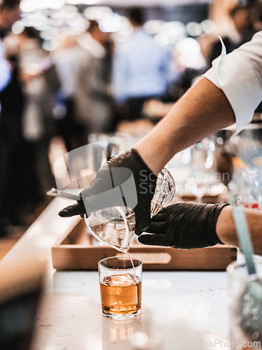 Image of Expert barman is making cocktail at business banquet event in hotel conference center. Blurred businesspeople at banquet event business meeting event in the background