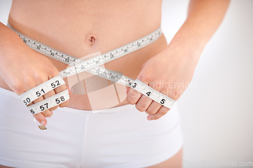 Image of Hands, body and woman with tape measure on abdomen in underwear for weight loss, health and wellness isolated on a white studio background. Closeup, stomach and girl measuring waist for diet or care