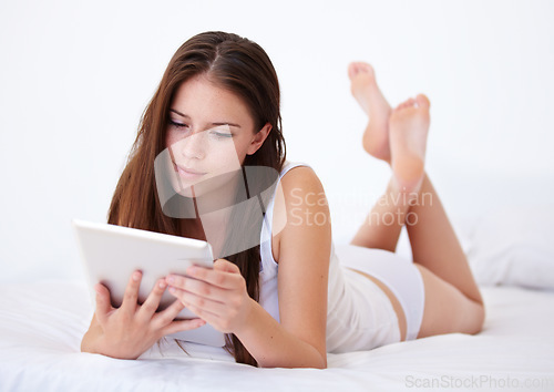 Image of Relax, tablet and app with a woman in the bedroom of her apartment for browsing on the weekend. Technology, social media or streaming with a young person lying on a bed in her home for morning rest