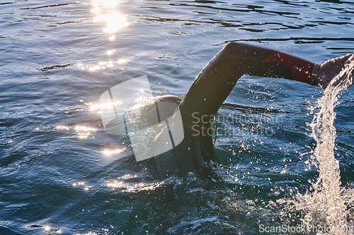 Image of Triathlon athlete swimming on lake in sunrise wearing wetsuit