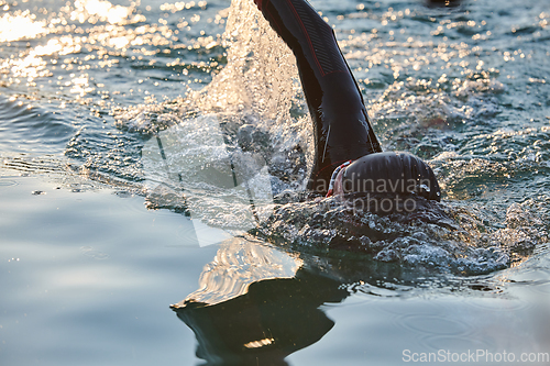 Image of Triathlon athlete swimming on lake in sunrise wearing wetsuit