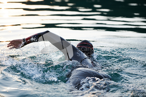 Image of Triathlon athlete swimming on lake in sunrise wearing wetsuit