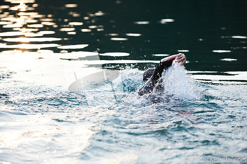 Image of Triathlon athlete swimming on lake in sunrise wearing wetsuit