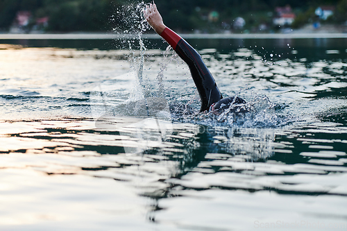 Image of Triathlon athlete swimming on lake in sunrise wearing wetsuit