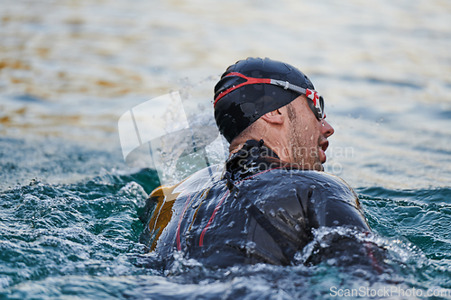 Image of Triathlon athlete swimming on lake in sunrise wearing wetsuit