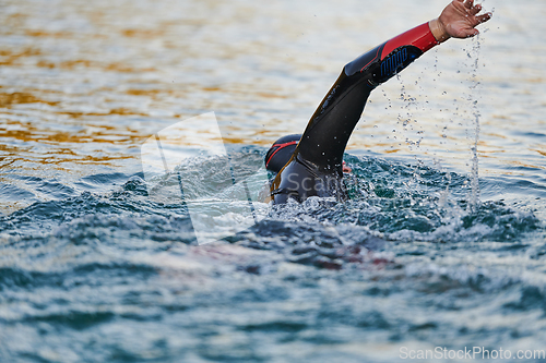 Image of Triathlon athlete swimming on lake in sunrise wearing wetsuit