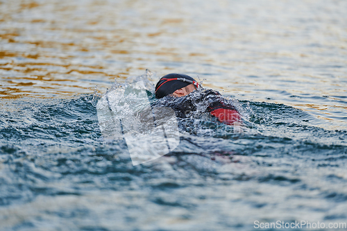 Image of Triathlon athlete swimming on lake in sunrise wearing wetsuit