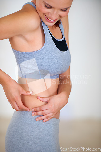 Image of Fitness, stomach and woman holding skin for health, wellness and weight loss goals in a training studio. Smile, happy and young female person athlete showing body for exercise or workout at gym.