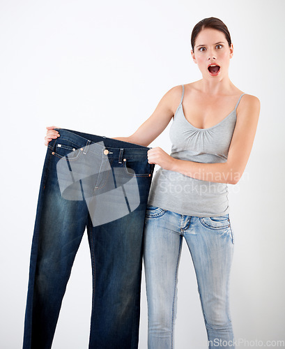 Image of Diet, weight loss and woman with surprise from jeans, change in size or white background in studio. Shocked, portrait or person with crazy reaction to transformation in fitness or large denim pants