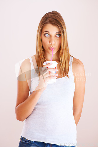 Image of Woman, drink and studio with cup of soda, fizzy cola and ice cold milkshake isolated on white background. Thirsty young girl, thinking and sip straw for takeaway beverage, juice or fast food smoothie