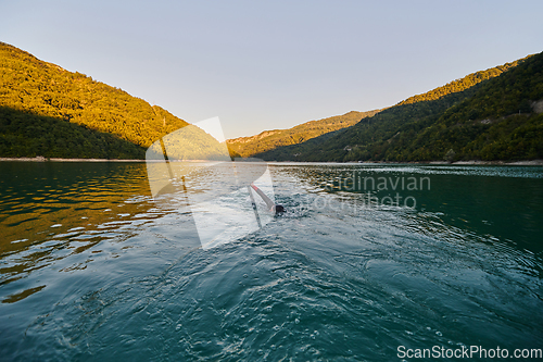 Image of Triathlon athlete swimming on lake in sunrise wearing wetsuit