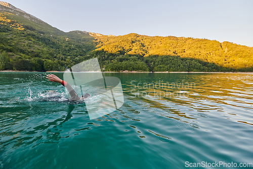 Image of Triathlon athlete swimming on lake in sunrise wearing wetsuit