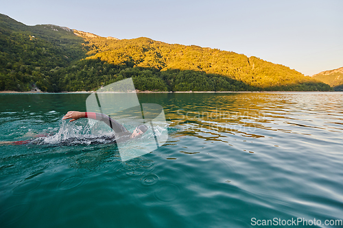 Image of Triathlon athlete swimming on lake in sunrise wearing wetsuit