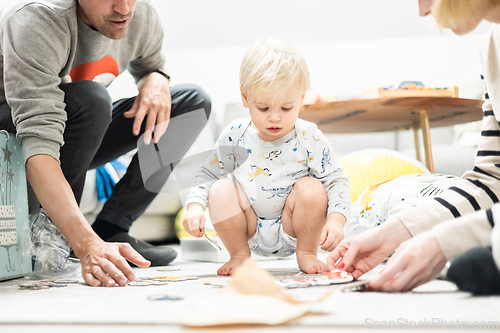 Image of Parents playing games with child. Little toddler doing puzzle. Infant baby boy learns to solve problems and develops cognitive skills. Child development concept