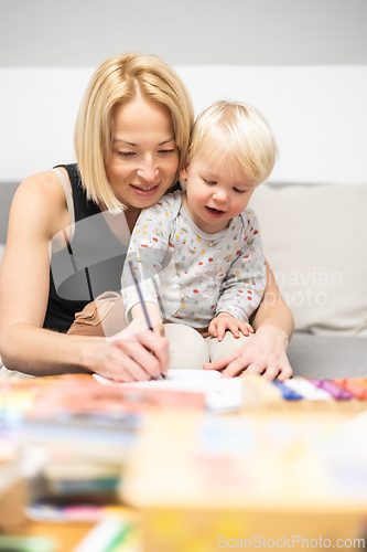 Image of Caring young Caucasian mother and small son drawing painting in notebook at home together. Loving mom or nanny having fun learning and playing with her little 1,5 year old infant baby boy child.