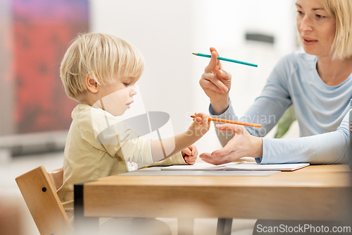 Image of Caring young Caucasian mother and small son drawing painting in notebook at home together. Loving mom or nanny having fun learning and playing with her little 1,5 year old infant baby boy child.