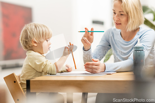 Image of Caring young Caucasian mother and small son drawing painting in notebook at home together. Loving mom or nanny having fun learning and playing with her little 1,5 year old infant baby boy child.