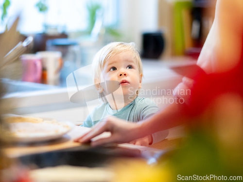 Image of Mother and little toddler baby boy making pancakes for breakfast together in domestic kitchen. Family, lifestyle, domestic life, food, healthy eating and people concept.