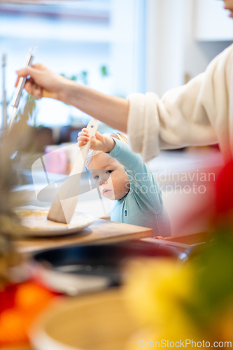 Image of Mother and little toddler baby boy making pancakes for breakfast together in domestic kitchen. Family, lifestyle, domestic life, food, healthy eating and people concept.