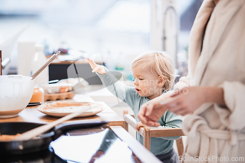 Image of Mother and little toddler baby boy making pancakes for breakfast together in domestic kitchen. Family, lifestyle, domestic life, food, healthy eating and people concept.