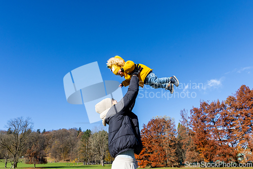 Image of More, more,...mum, that's fun. Happy young mother throws her cute little baby boy up in the air. Mother's Day, Mather and her son baby boy playing and hugging outdoors in nature in fall.