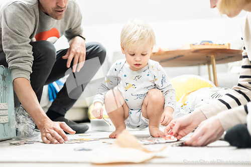 Image of Parents playing games with child. Little toddler doing puzzle. Infant baby boy learns to solve problems and develops cognitive skills. Child development concept