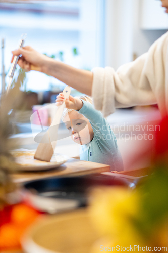 Image of Mother and little toddler baby boy making pancakes for breakfast together in domestic kitchen. Family, lifestyle, domestic life, food, healthy eating and people concept.