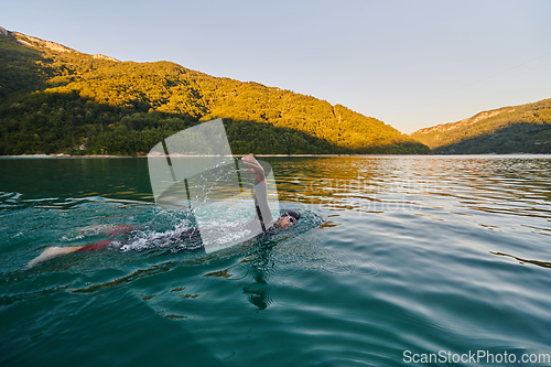 Image of Triathlon athlete swimming on lake in sunrise wearing wetsuit