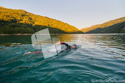 Image of Triathlon athlete swimming on lake in sunrise wearing wetsuit