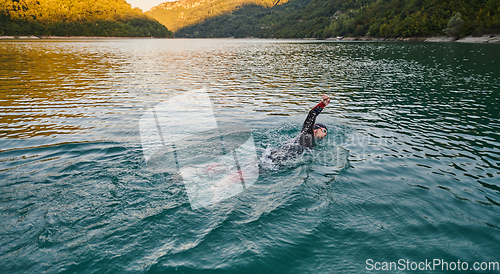 Image of Triathlon athlete swimming on lake in sunrise wearing wetsuit