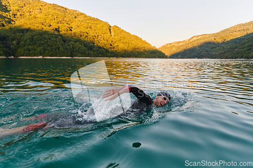Image of Triathlon athlete swimming on lake in sunrise wearing wetsuit