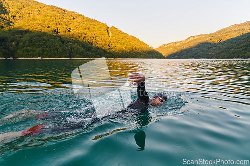 Image of Triathlon athlete swimming on lake in sunrise wearing wetsuit