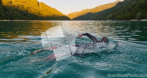 Image of Triathlon athlete swimming on lake in sunrise wearing wetsuit