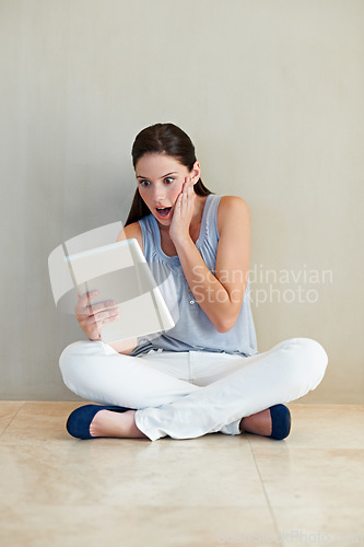 Image of Woman, tablet and surprised on social media, news or gossip sitting against a wall at home. Shocked female person, brunette or freelancer gasping on technology for notification, alert or information