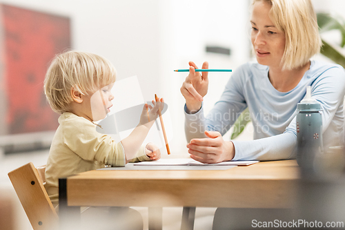 Image of Caring young Caucasian mother and small son drawing painting in notebook at home together. Loving mom or nanny having fun learning and playing with her little 1,5 year old infant baby boy child.