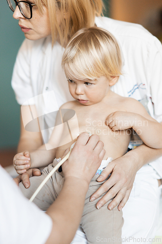 Image of Small child being checked for heart murmur by heart ultrasound exam by cardiologist as part of regular medical checkout at pediatrician.