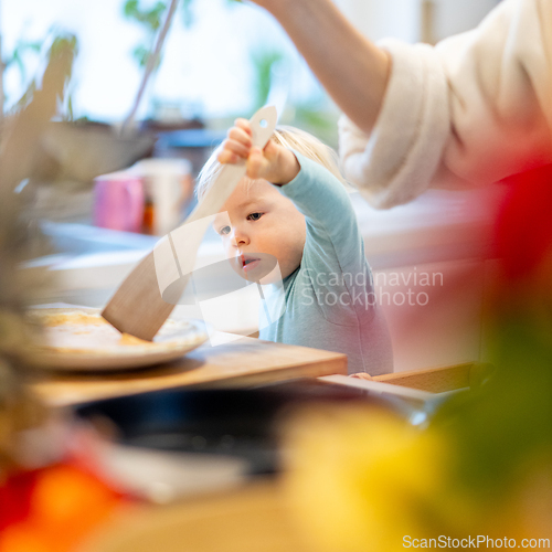 Image of Mother and little toddler baby boy making pancakes for breakfast together in domestic kitchen. Family, lifestyle, domestic life, food, healthy eating and people concept.