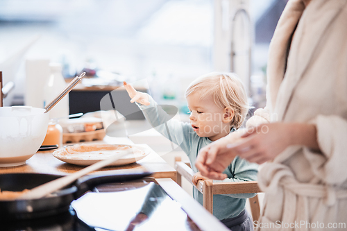 Image of Mother and little toddler baby boy making pancakes for breakfast together in domestic kitchen. Family, lifestyle, domestic life, food, healthy eating and people concept.