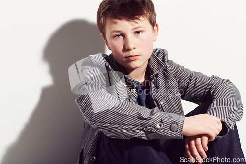 Image of Serious, boy and portrait of teenager with fashion in studio, white background or mockup. Child, sitting and relax in cool style and clothes with confidence, pride and hipster personality in space