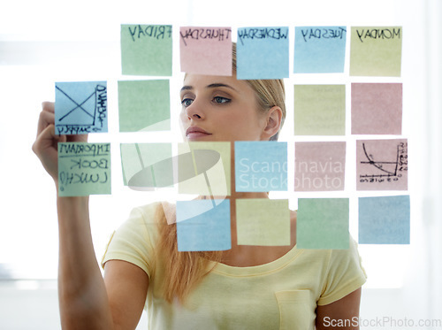 Image of Woman, writing on sticky notes and glass wall with schedule, serious and planning. Copywriter, brainstorming and office job with calendar, workplace and moodboard for ideas, content plan and creative