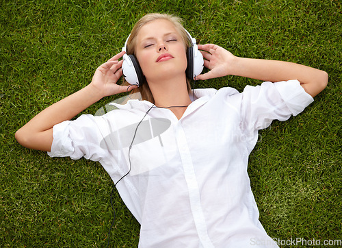 Image of Woman, relax on grass and listening to music with audio streaming service and mental health in park or garden. Young student sleeping or dream of electronics with headphones on lawn or floor above