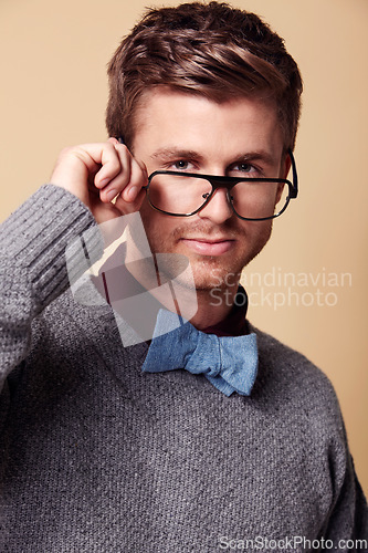 Image of Portrait, glasses and bowtie for fashion with a man in studio on a tan background for vision or style. Face, eyewear and accessories with a confident young geek or nerd in a casual clothing outfit