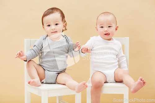 Image of Portrait, chair and baby boys for growth or child development in studio on an orange background. Children, cute or adorable and sibling or small infant kids sitting together for family bonding