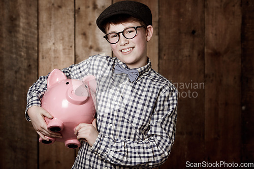 Image of Young child, piggy bank or smile in portrait by wooden background, money saving or growth in youth in retro fashion. Boy, smile and face for coin banking and safe for bills with glasses by backdrop